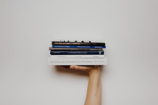 Hand holding a stack of books against a minimal white background, perfect for educational themes.